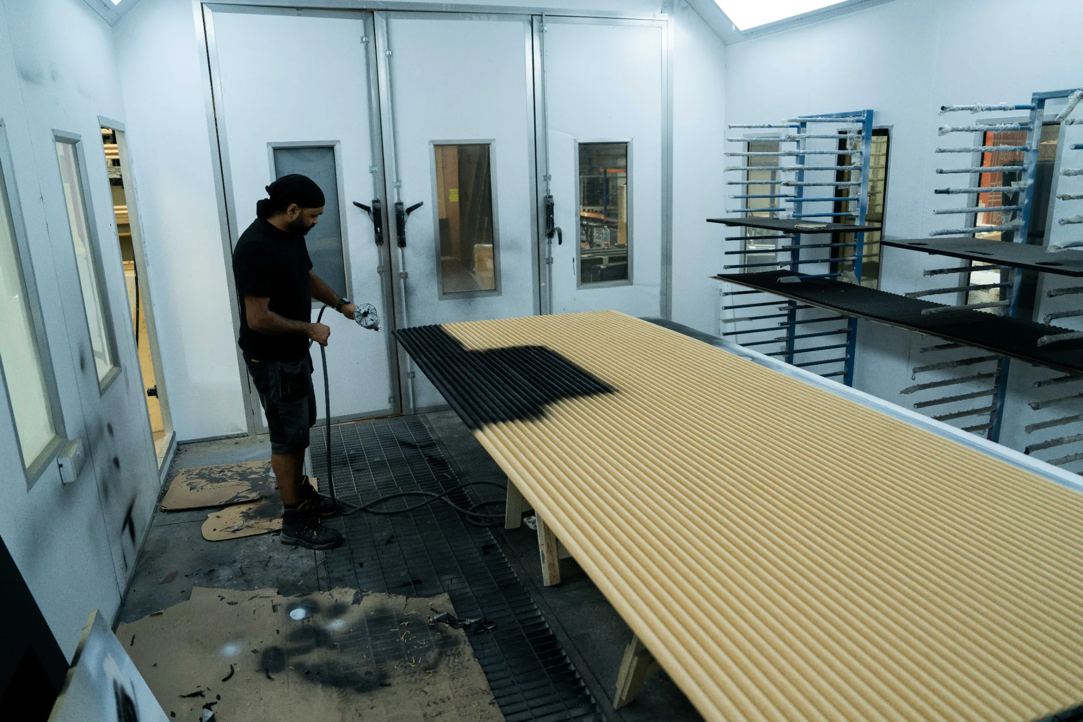 Operator spray finishing a long panel inside the CNC Production spray booth