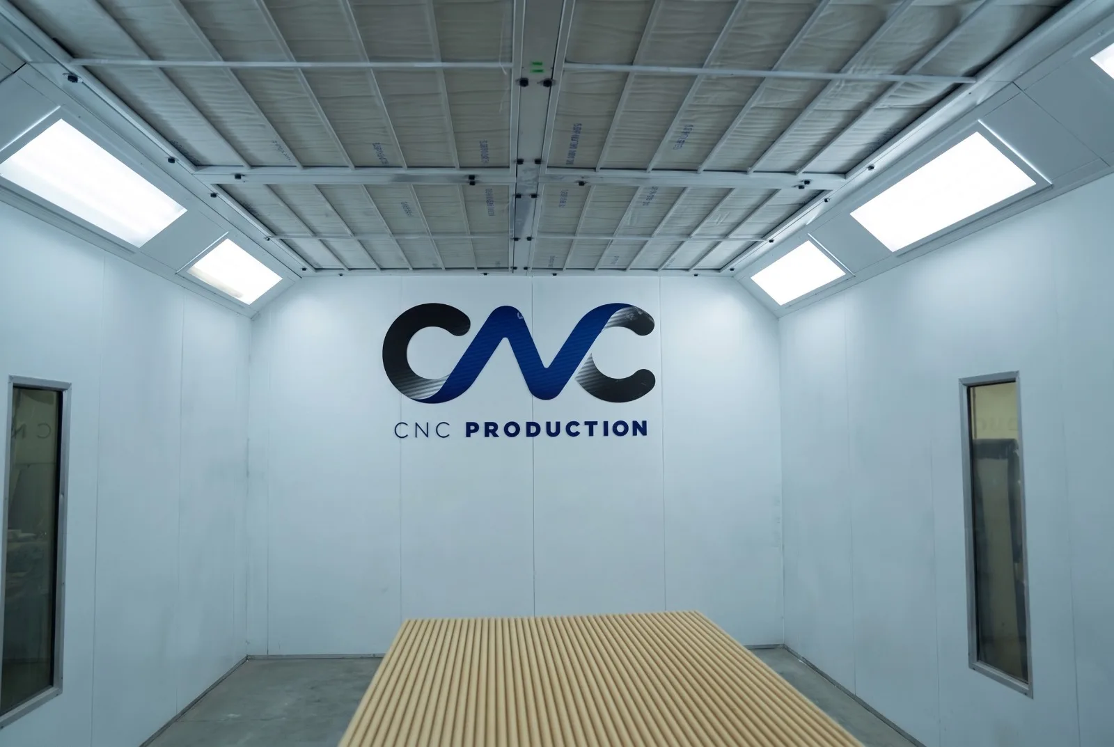 CNC Production spray booth interior with the CNC Production logo on the back wall and a panel ready to finish